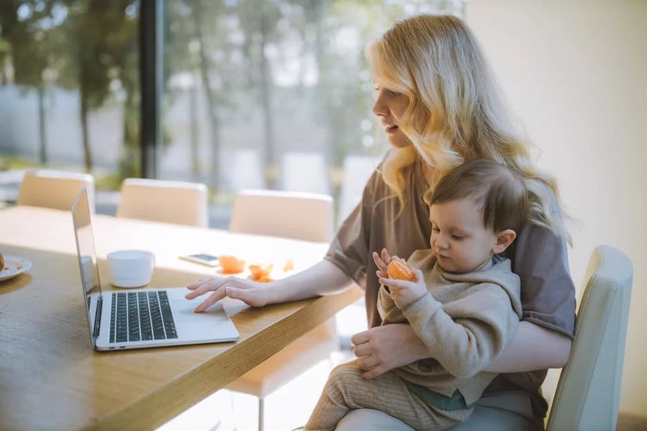 Mother checking email with child on lap eating an orange